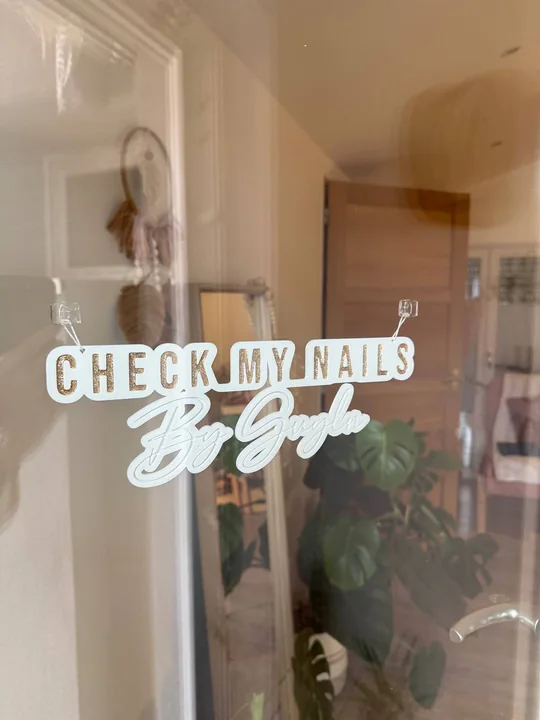 Enseigne « Check my nails » imprimée en 3D, suspendue derrière une vitre