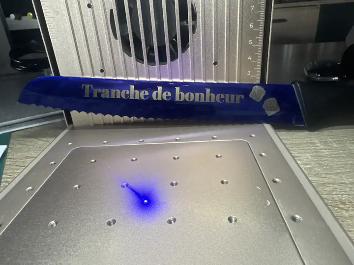 Couteau à pain en cours de gravure, sous le faisceau laser bleu