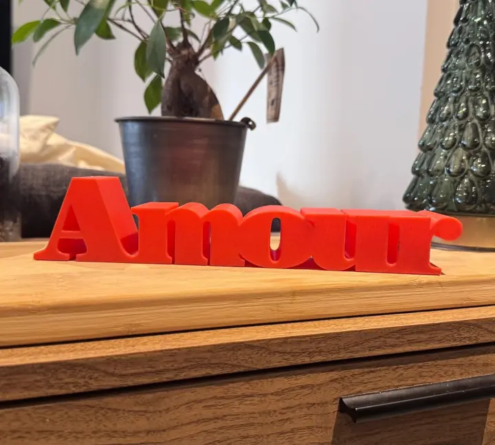 Mot « Amour » en lettres rouges imprimées en 3D, posé sur une planche en bois