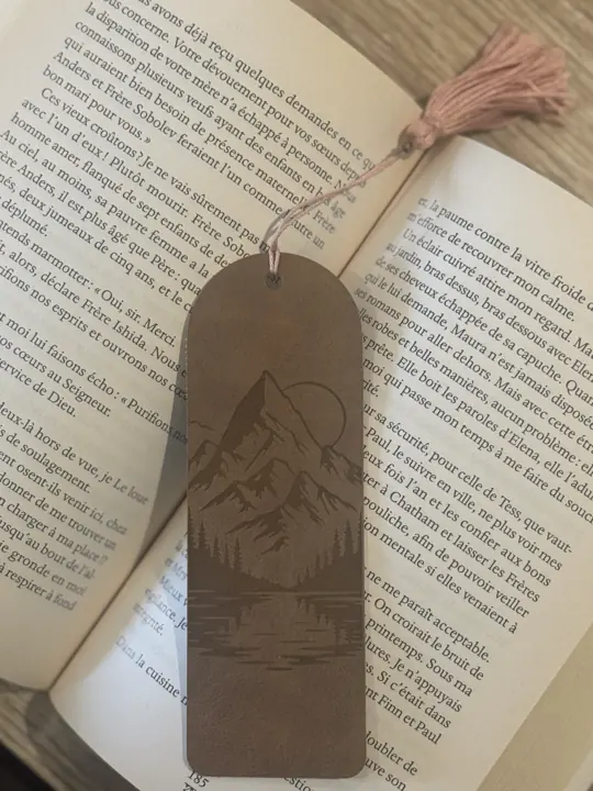 Marque-page en cuir gravé d’un paysage de montagne, glissé dans un livre